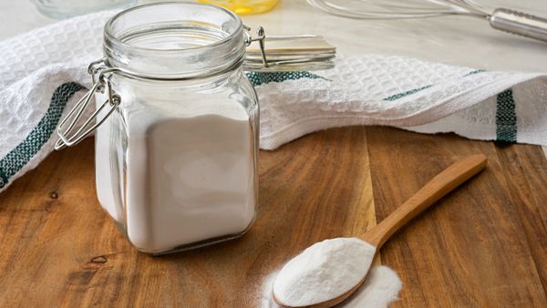 A jar of baking soda beside a spoon filled with baking soda.