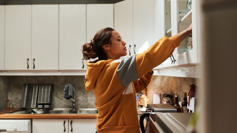 A woman opening a kitchen cabinet. 