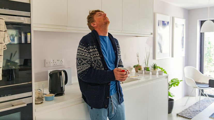 A man standing and holding a cup in his kitchen while looking breathless. 