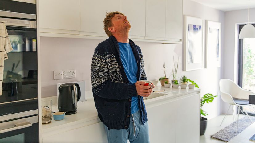 A man standing and holding a cup in his kitchen while looking breathless.