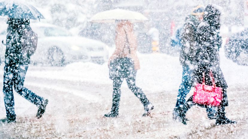 Pedestrians crossing the street on a snowy day. 