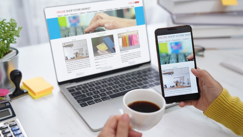 Woman checking a shopping website on her laptop while holding her phone. 