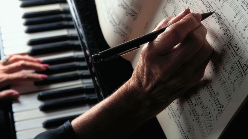 A man writing down music while using a musical keyboard. 