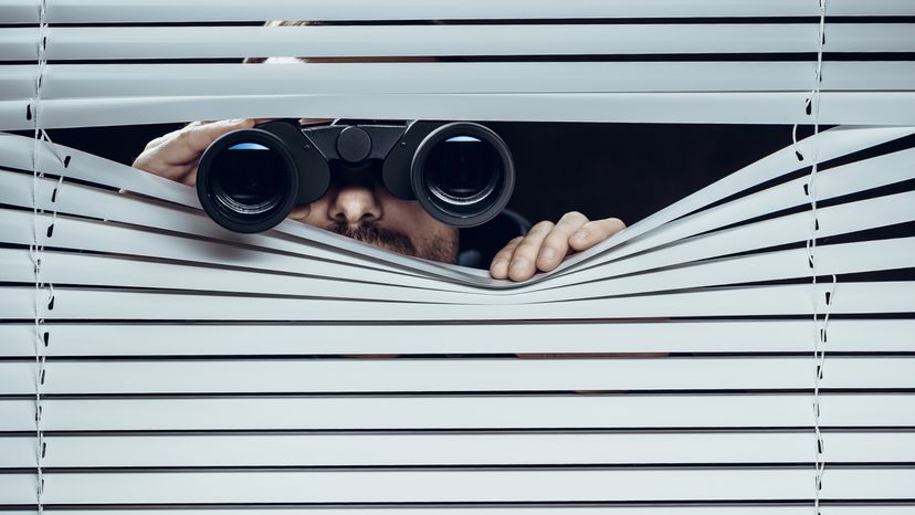 A man looking out from a window with binoculars. 