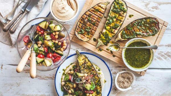 A colorful spread of grilled eggplant, herb butter, and salad on a table. 