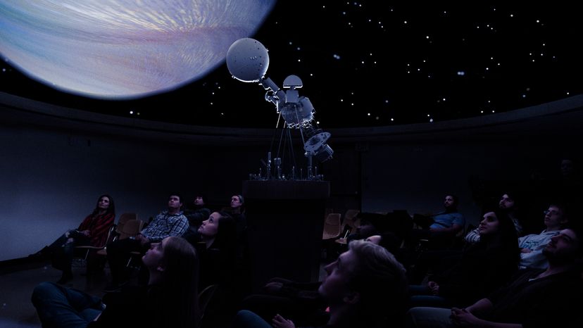 A group of people sitting and watching the galaxy through a planetarium. 