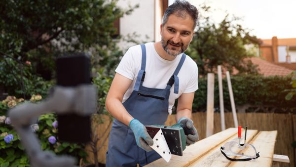 A carpenter using his phone placed on a tripod to record an online tutorial. 