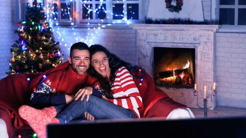 A young couple wearing Christmas inspired pyjamas while watching a movie. 