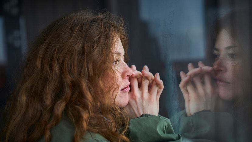 A red haired woman sitting and staring out a window. 