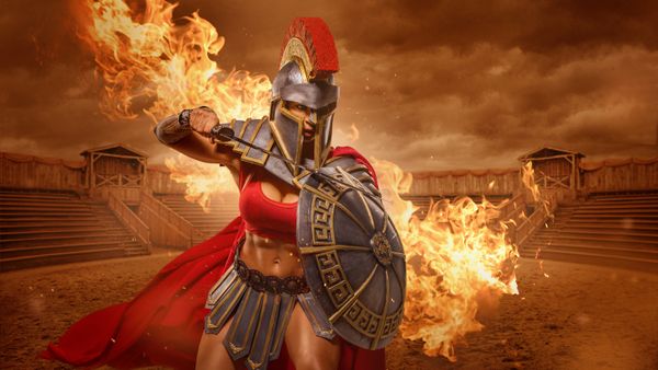 An image of a woman in gladiator outfit, holding a weapon. 