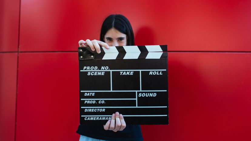 A young girl holding a movie clapboard in front of a red background. 