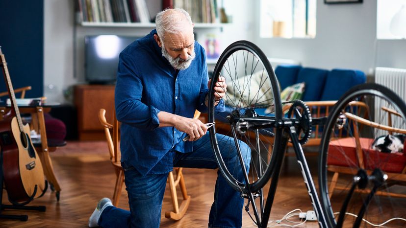 Man in his 50s at home with upside down bicycle repairing it.