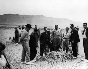 Manhattan Project officials, including Dr. Robert J. Oppenheimer (white hat) and General Leslie Groves, inspect the detonation site of the Trinity atomic bomb test.