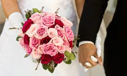 Bride and groom holding hands, bride holding bouquet, mid section