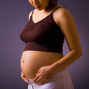 Studio shot of a pregnant woman standing over grey background with her stomach exposed