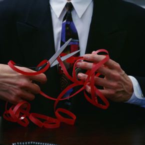 businessman cutting through red tape with scissors