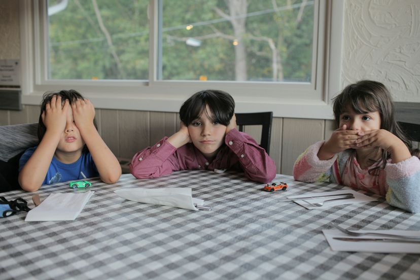 Three kids with a middle child in the center covering his ears