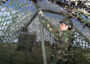 An airman in the U.S. Air Force covers military trucks with camouflage netting.