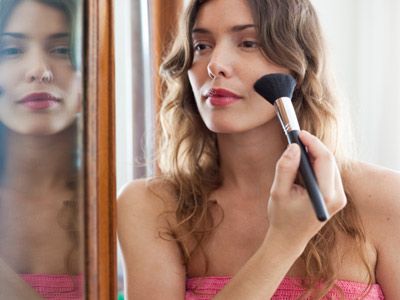 Woman applying makeup in mirror. 