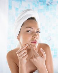 Woman examines pimple in mirror.