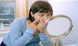 Woman examining face in mirror.