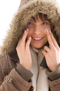 Portrait of young smiling woman in fur hooded jacket, applying moisturizer to cheek
