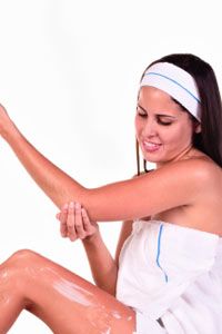 Young woman massaging and applying a moisturizer to her elbow.
