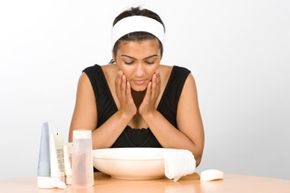 A young Indian woman washes her face. She has creams and toner next to her wash bowl.