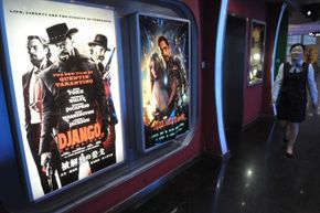A woman walks past movie posters at a movie theater. 