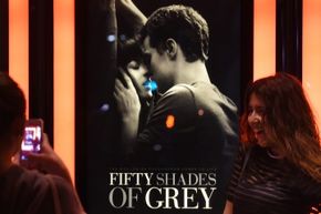 A woman poses for a photo in front of a "Fifty Shades of Grey" movie poster. 