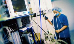 A woman in scrubs, hair net and mask adjusts one of many pieces of medical equipment in an operating room.