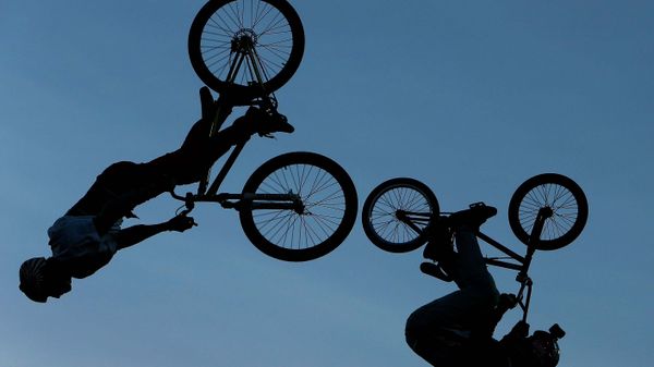 Silhouetted cyclist rides back lit bicycle.