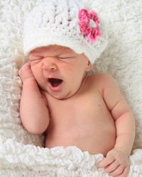 A newborn baby girl in a white and pink hat.