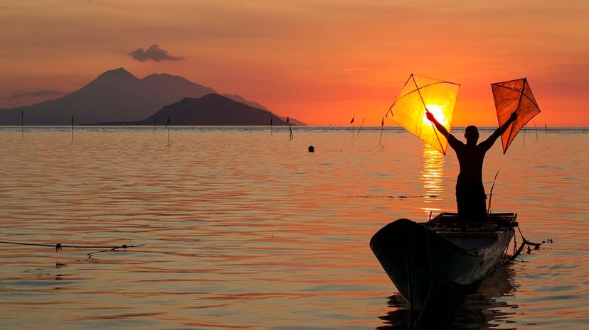 man standing in boat with kites