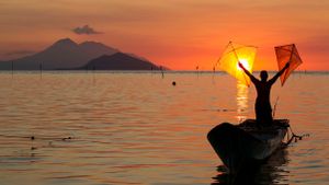 man standing in boat with kites