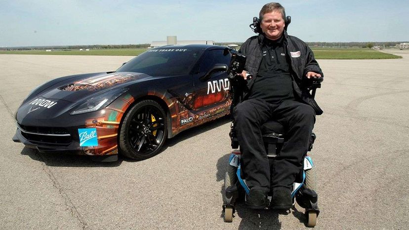 这张照片拍摄于2014年，瘫痪的赛车手山姆·施密特(Sam Schmidt)在他改装过的科吉特(Corgette)前，最近他获得了史无前例的驾照。美国空军/ Al明亮”width=