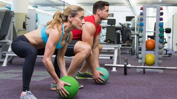 man and woman in gym squatting with medicine balls