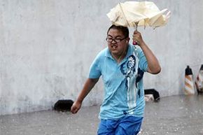 一个男人在被淹没的街道在长沙,中国在2013年。台风引发的洪水和泥石流Utor湖南造成9人死亡。”width=