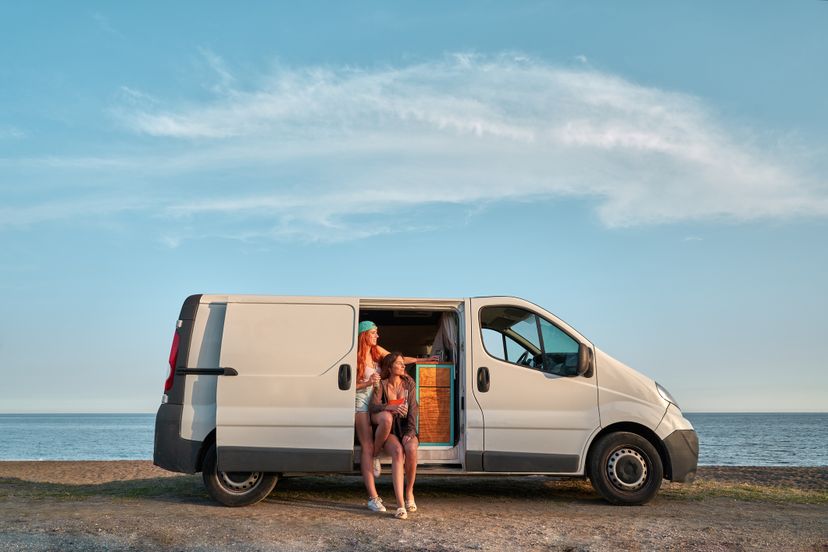 Two girls sitting in their camper van enjoying a few beers at sunset. Road trips and nomadic life.