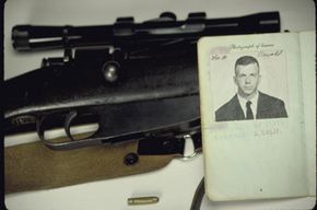 A photo of Lee Harvey Oswald pasted into a notebook, laying open on top of a gun.