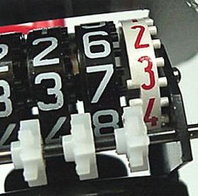 On the white wheel between the "3" and the "4," there are two pegs. One time per revolution, one of the gear teeth on the white gear falls in between these two pegs, causing the black gear next to it to move one-tenth of a revolution.”border=