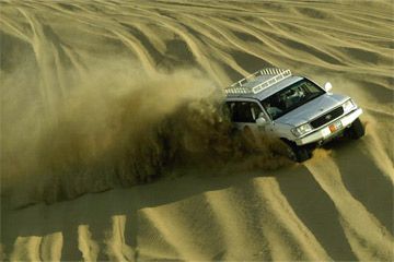Car speeds through outdoor extreme sports in a dust cloud.