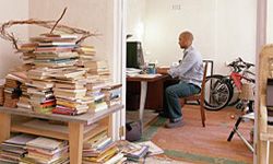 A man sitting at a desk in his home office surrounded by clutter.&nbsp;