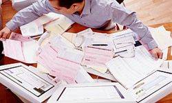 A man sitting at a messy desk that is covered in piles of papers.&nbsp;