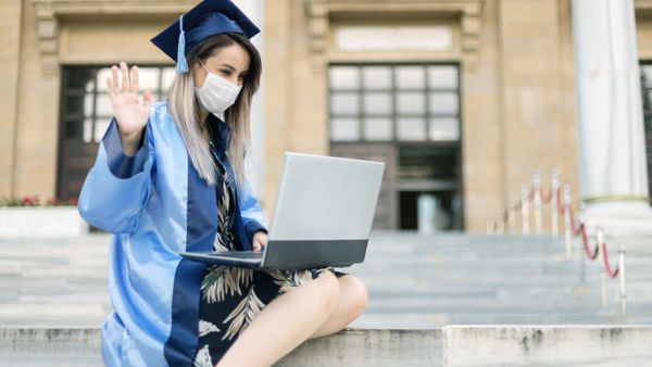 A young woman wearing a graduation dress while on a laptop