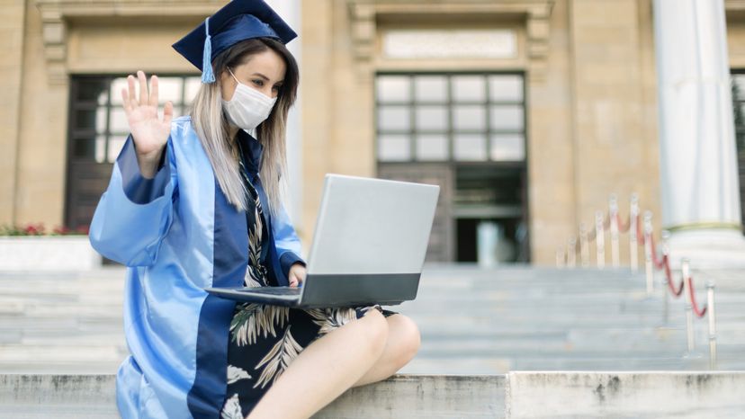A young woman wearing a graduation dress while on a laptop