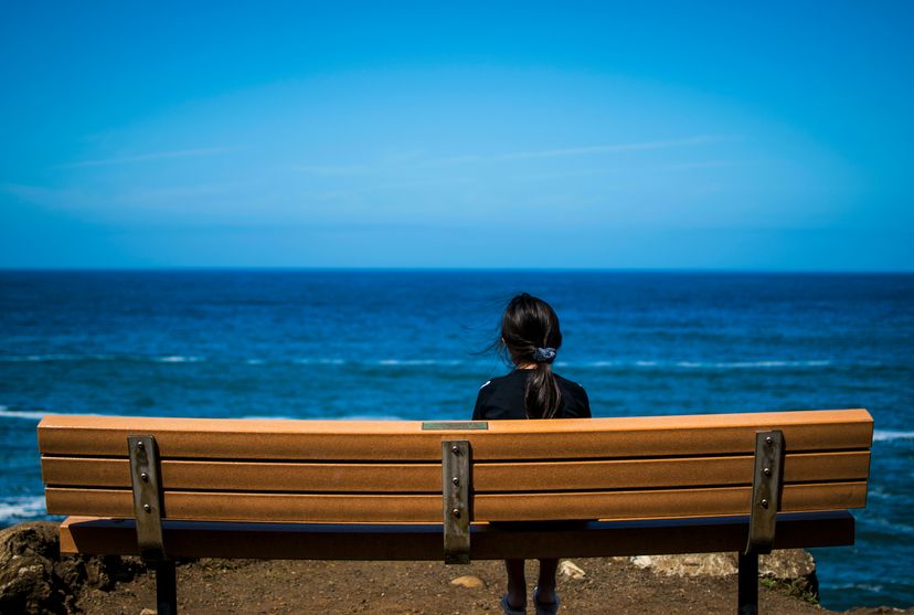 Only child sitting on a bench overlooking the ocean