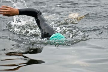 Person swimming outdoors in water wearing a wetsuit.