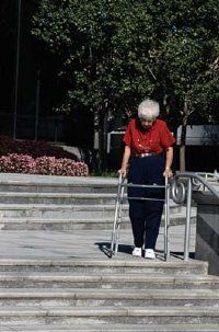 An elderly woman with a walker attempting to descend a set of stairs.&nbsp;