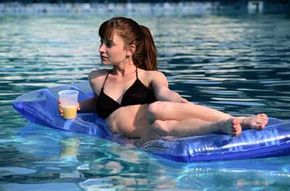 A young woman in a pool, relaxing with a drink on a swimming float.&nbsp;